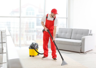 Male worker cleaning carpet with vacuum in living room