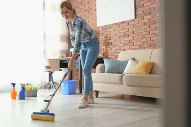 Photo of Woman cleaning floor with mop in living room