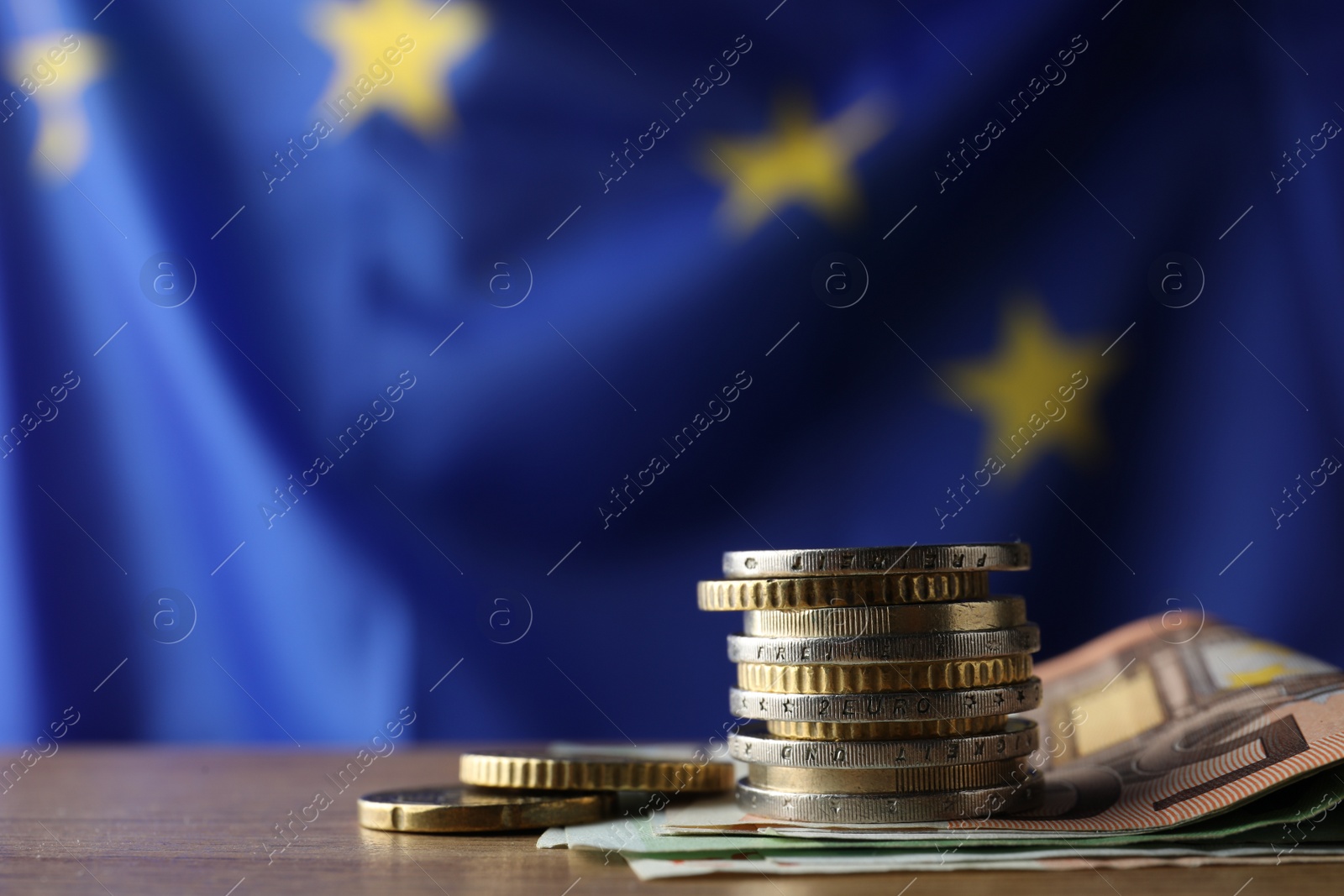 Photo of Coins and banknotes on wooden table against European Union flag, space for text