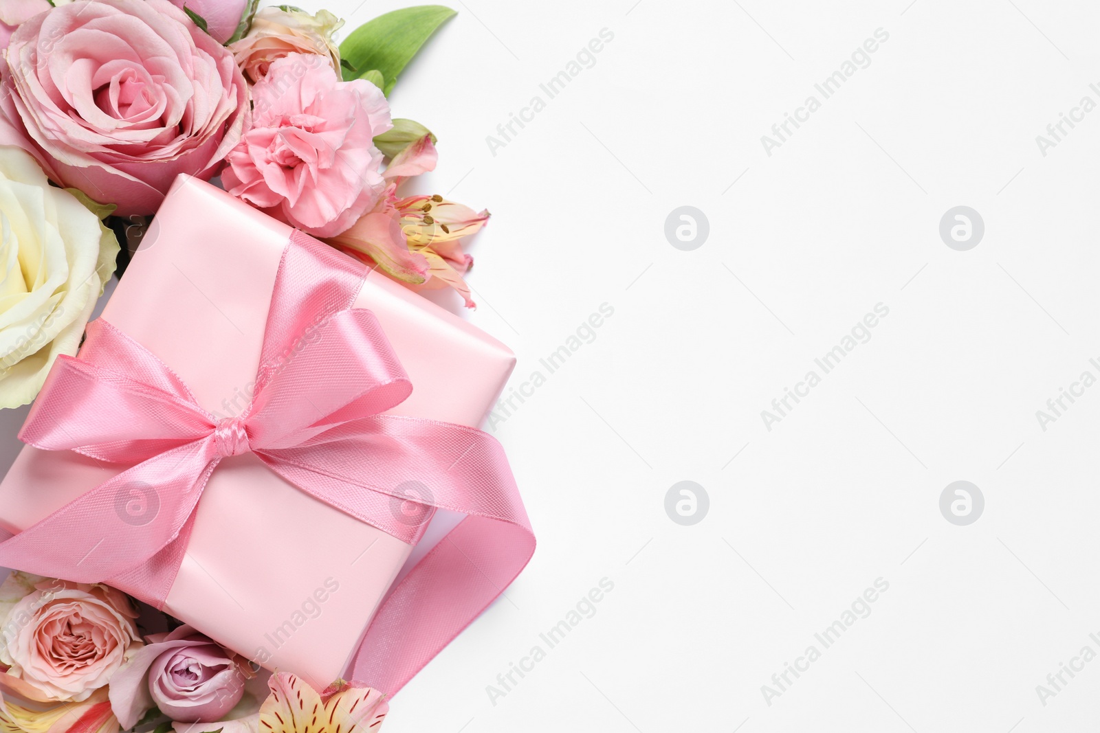 Photo of Gift box and beautiful flowers on white background, flat lay. Space for text