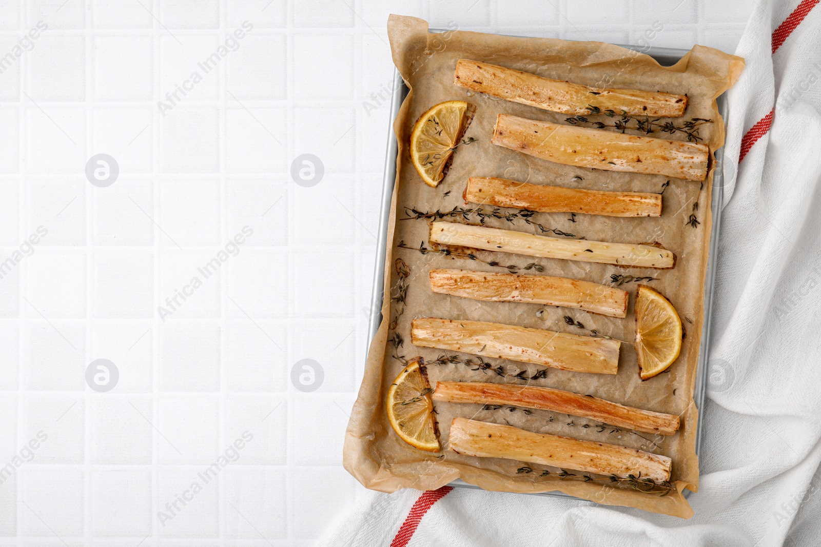 Photo of Baking tray with cooked salsify roots, lemon and thyme on white tiled table, top view. Space for text