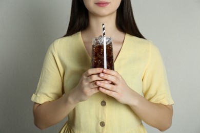 Woman holding glass of cola with ice and straw on beige background, closeup. Refreshing soda water