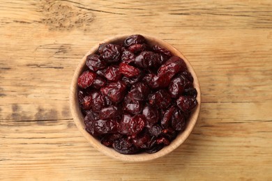 Photo of Tasty dried cranberries in bowl on wooden table, top view