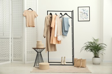 Photo of Rack with different stylish women's clothes, boots, bag and green houseplant indoors