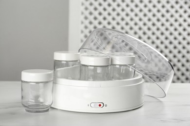 Modern yogurt maker with empty jars on white table indoors