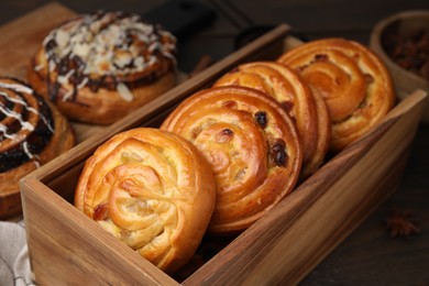 Delicious rolls with raisins in wooden box on table, closeup. Sweet buns