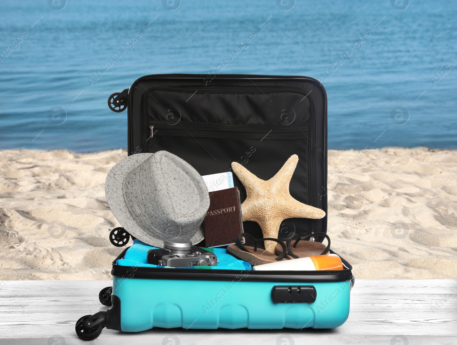 Image of Suitcase with different beach objects on grey wooden table near sea