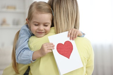 Photo of Little daughter congratulating her mom with greeting card at home. Happy Mother's Day