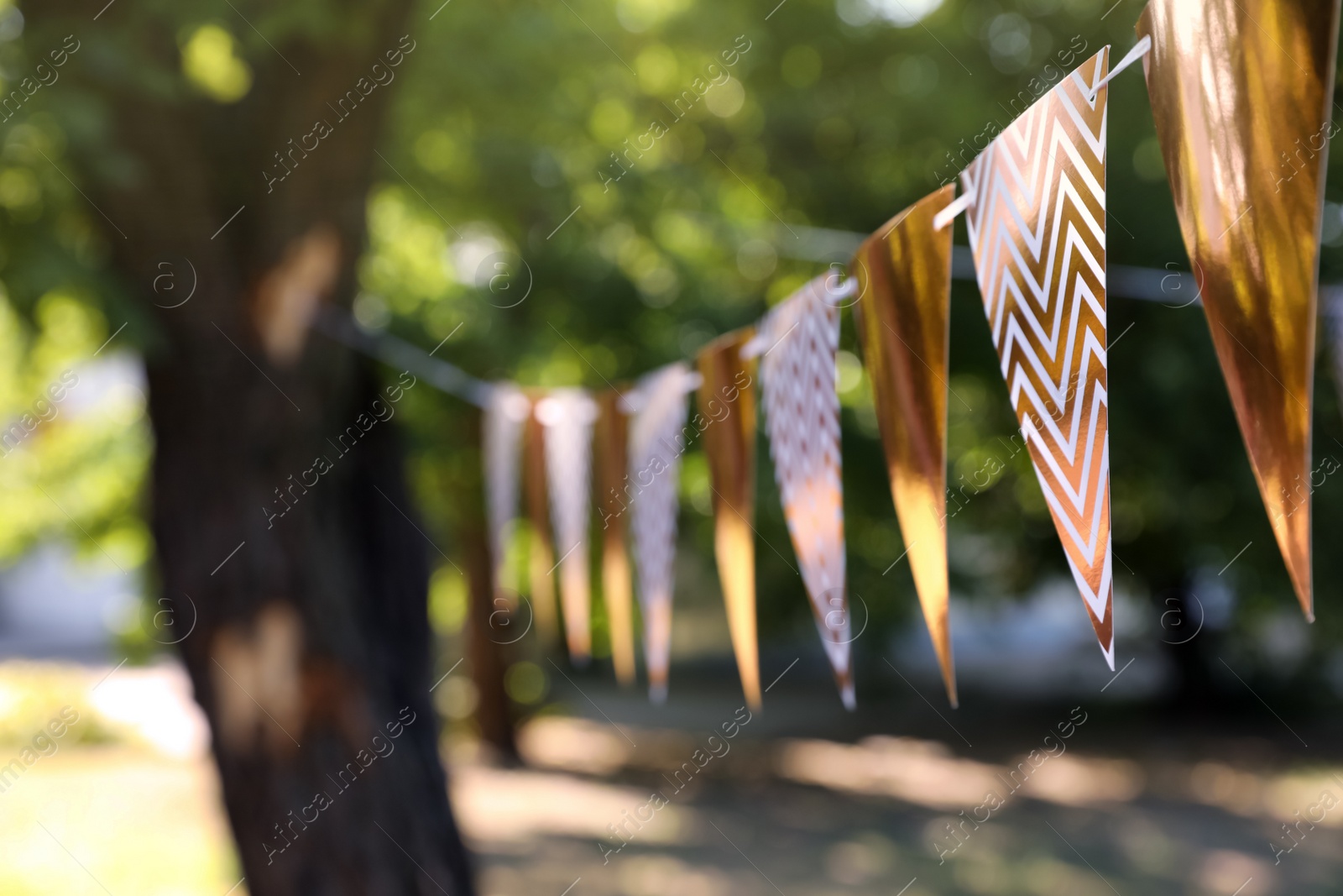 Photo of Golden bunting flags in park. Party decor