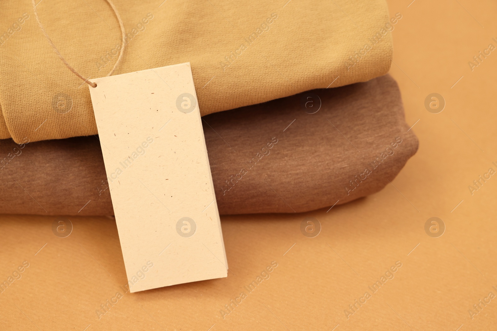 Photo of Garment with cardboard tag on kraft paper sheet, closeup. Space for text