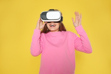 Emotional young woman playing video games with virtual reality headset on color background