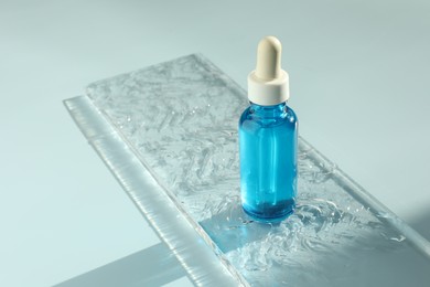 Bottle of cosmetic serum on light blue background, space for text