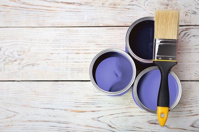 Image of Cans with violet paints and brush on white wooden background, top view. Space for text