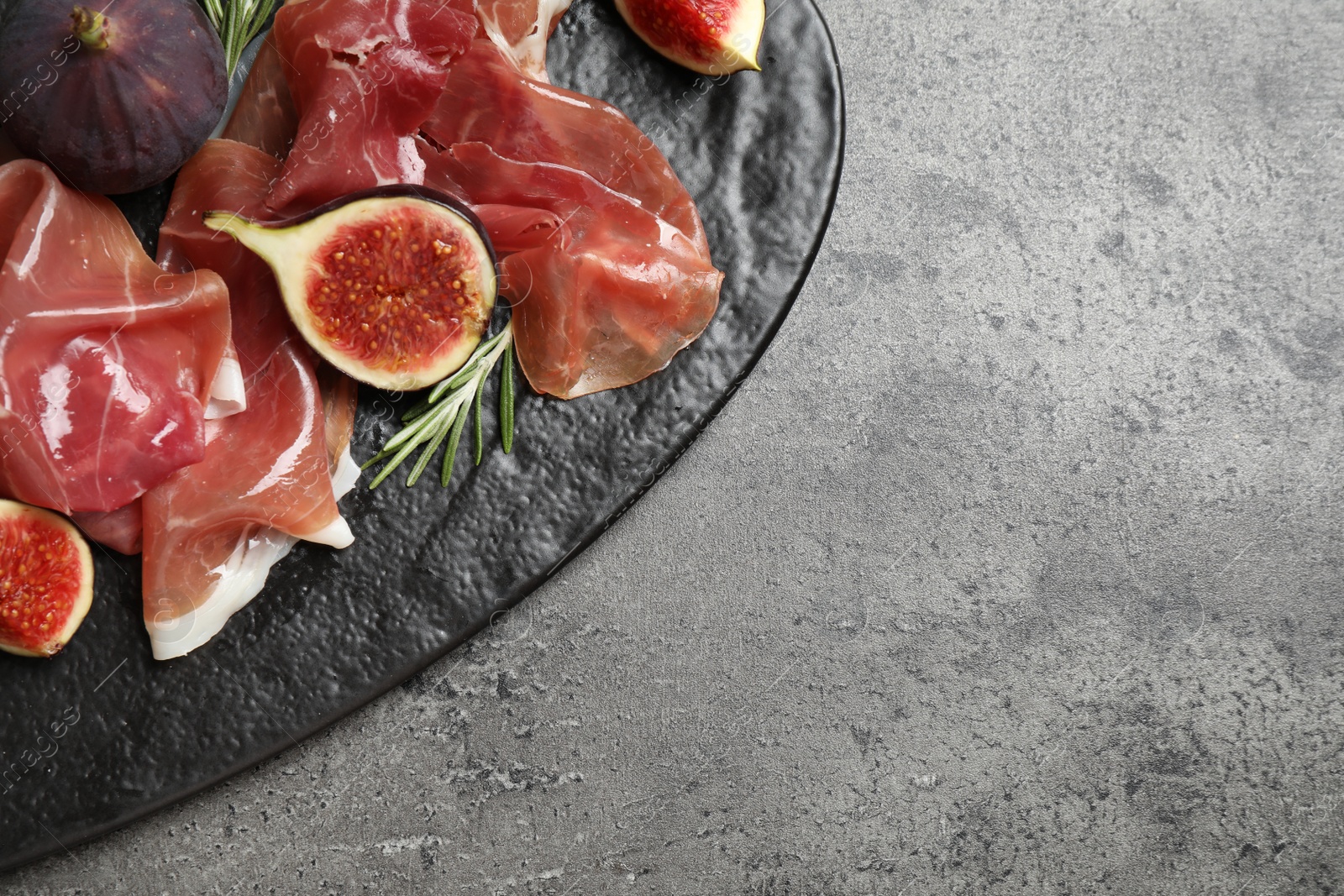 Photo of Delicious ripe figs and prosciutto served on grey table, top view. Space for text