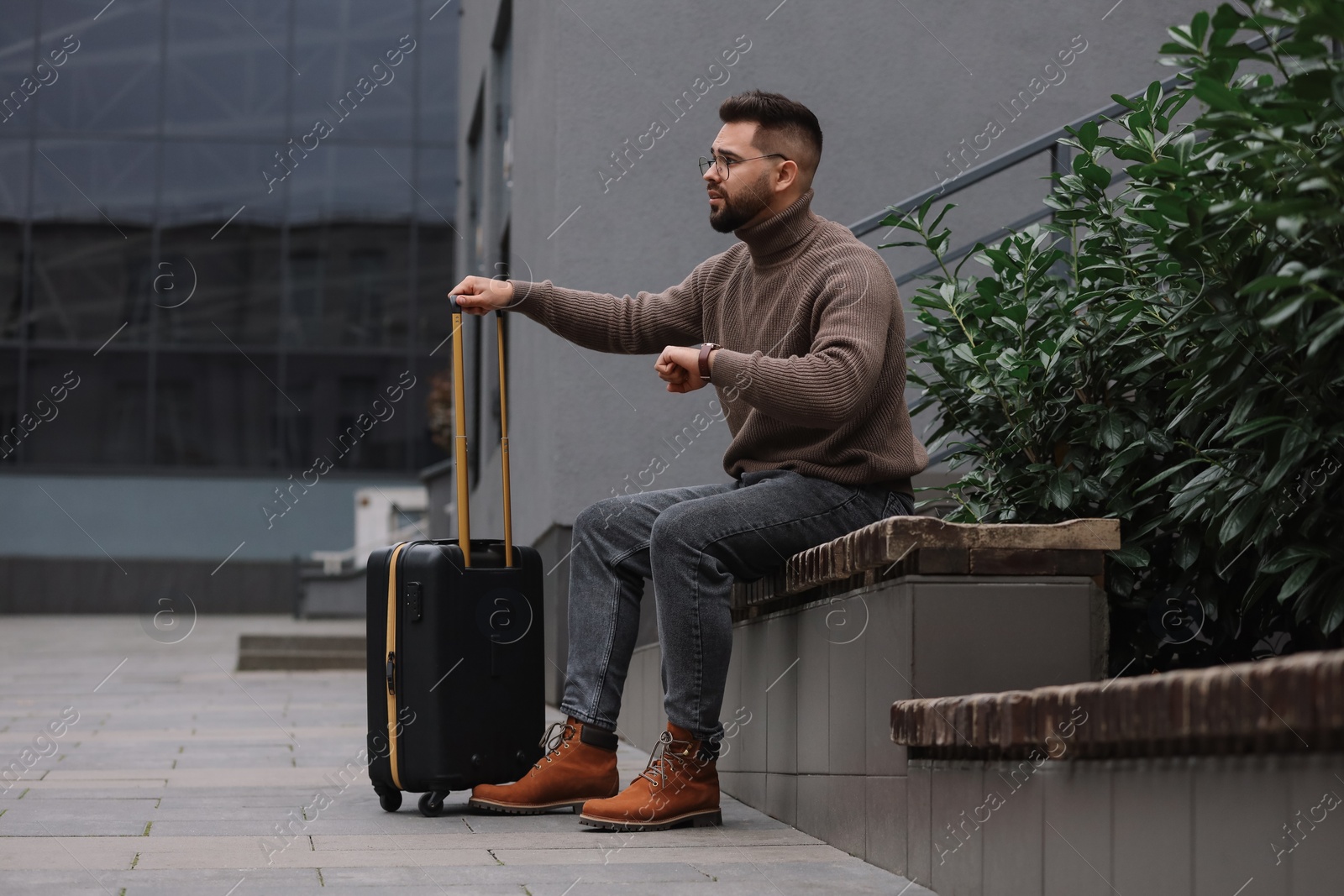 Photo of Being late. Worried man with suitcase sitting on bench outdoors, space for text