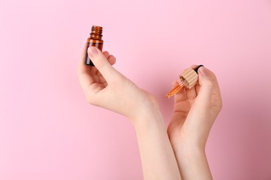 Photo of Woman applying essential oil onto wrist against pink background, closeup