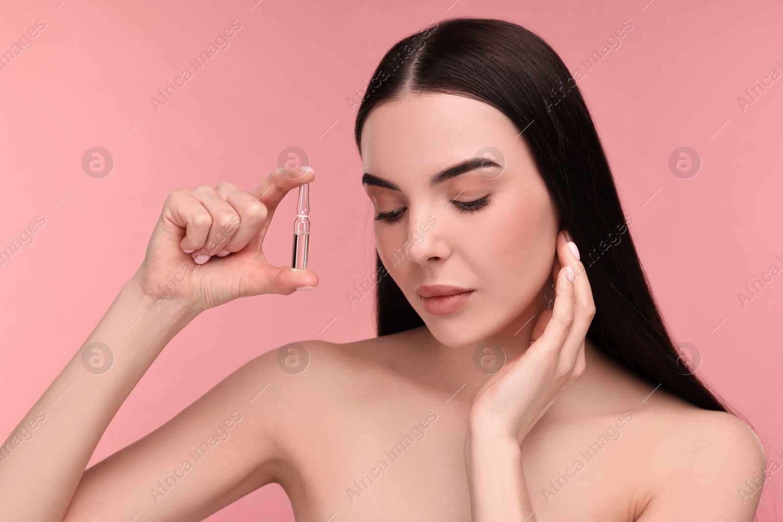 Photo of Beautiful young woman holding skincare ampoule on pink background