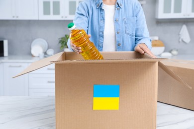 Humanitarian aid for Ukraine. Woman putting bottle of oil in donation box at white table indoors, closeup