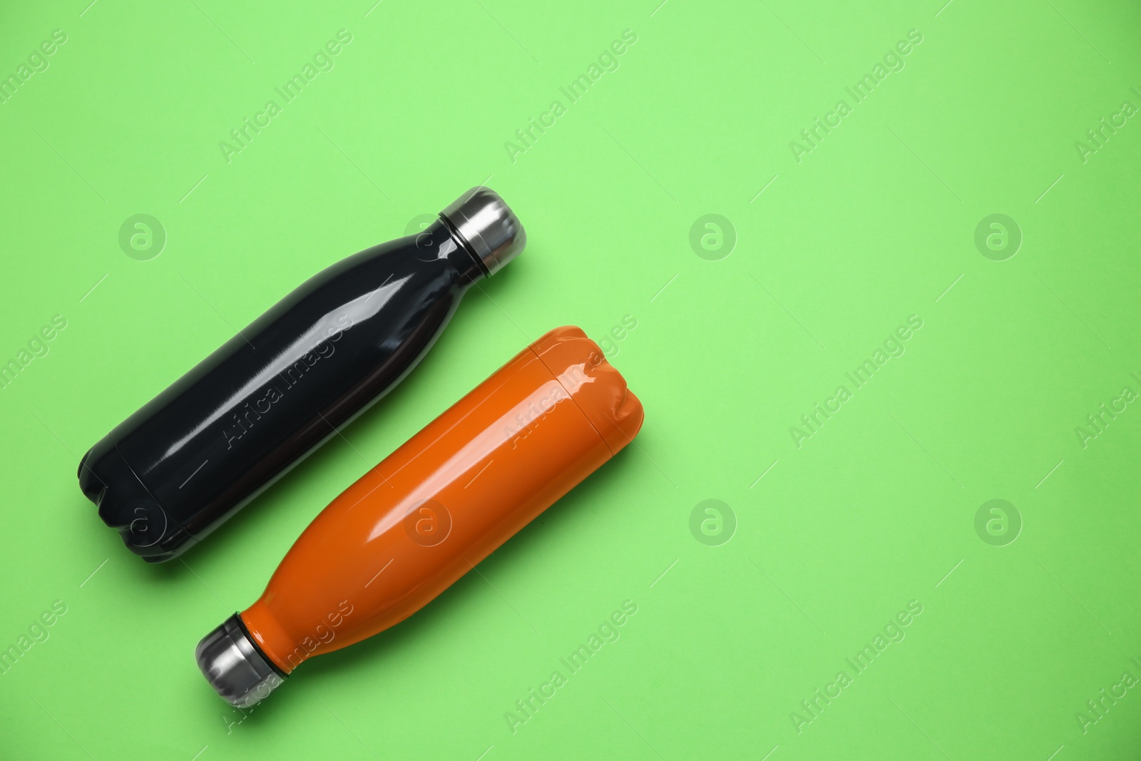 Photo of Different thermo bottles on green background, flat lay. Space for text