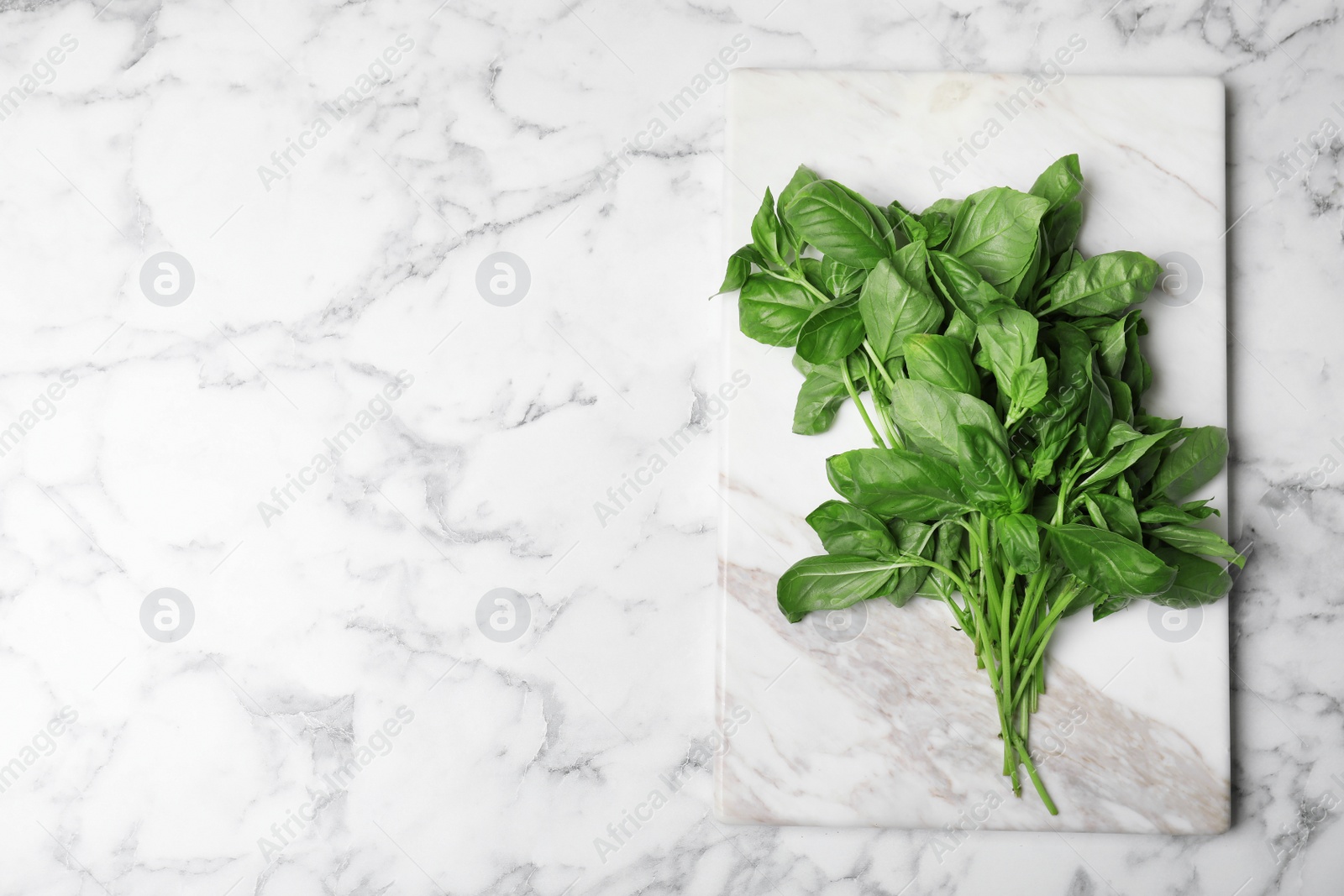 Photo of Stone board with basil leaves and space for text on marble background, top view