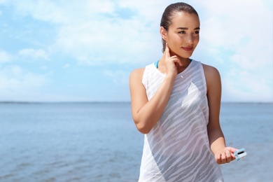 Photo of Young woman checking pulse with medical device after training on beach. Space for text