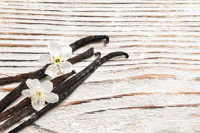 Photo of Vanilla sticks and flowers on wooden background