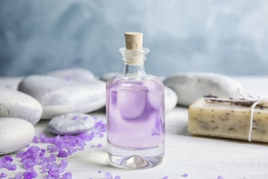 Photo of Bottle with natural herbal oil, soap and lavender flowers on table against blurred background