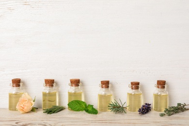 Glass bottles with different essential oils and herbs on wooden background