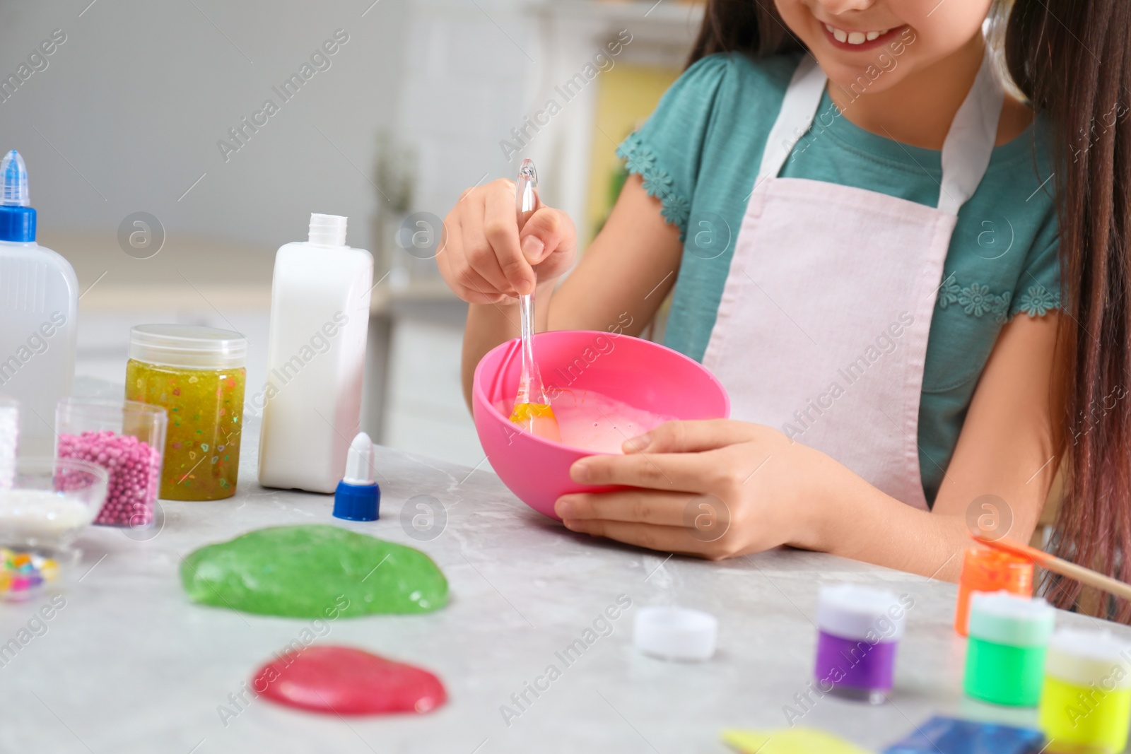 Photo of Little girl mixing ingredients with silicone spatula at table in kitchen, closeup. DIY slime toy