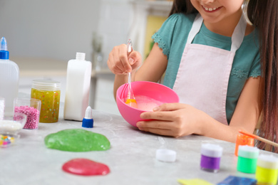 Photo of Little girl mixing ingredients with silicone spatula at table in kitchen, closeup. DIY slime toy