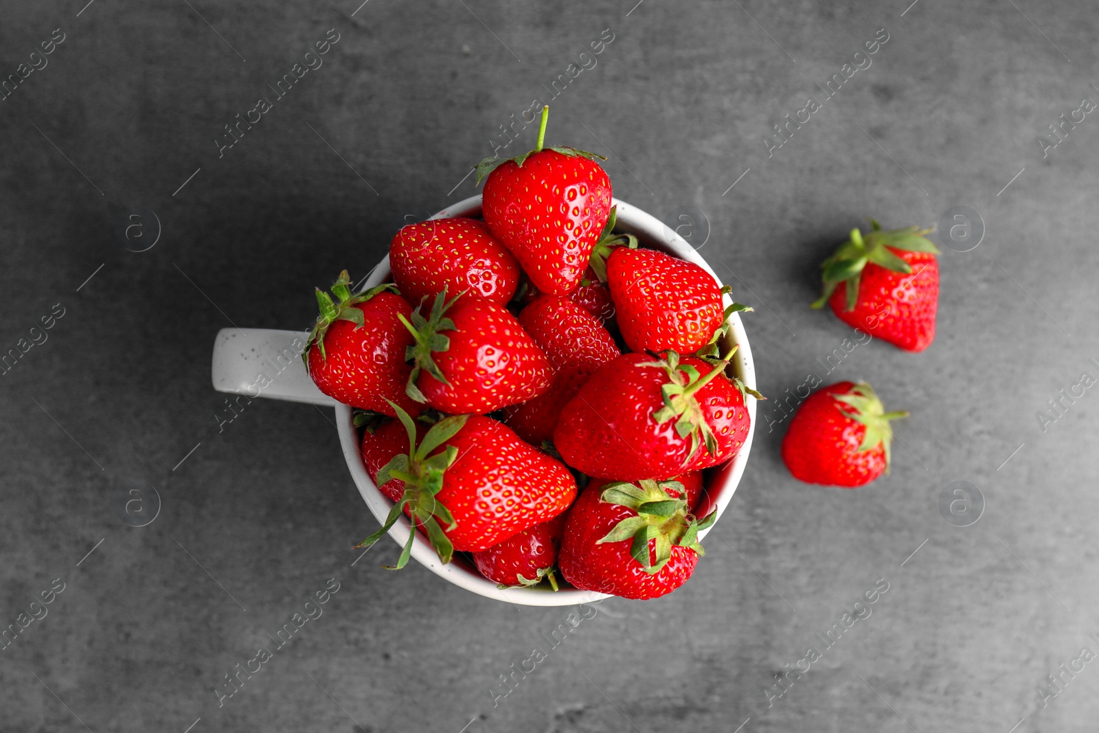 Photo of Mug with ripe red strawberries on grey background, top view