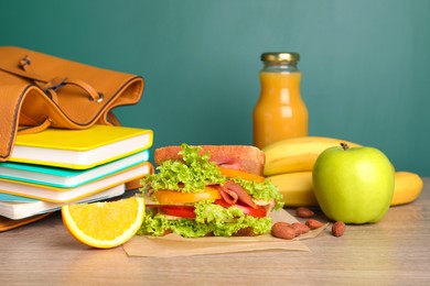 Photo of Tasty healthy food and different stationery on wooden table near green chalkboard. School lunch