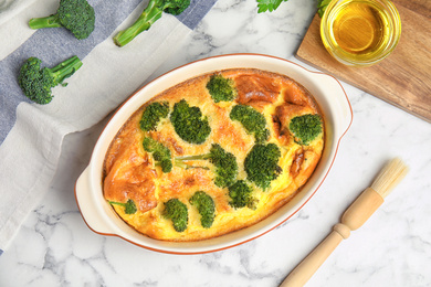 Tasty broccoli casserole in baking dish on white marble table, flat lay