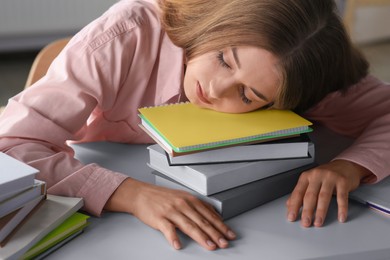 Young tired woman sleeping near books at white table