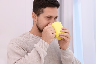 Man drinking from yellow mug at home