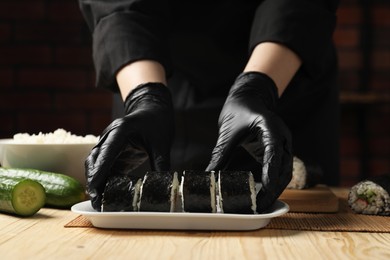 Photo of Chef in gloves making sushi rolls at wooden table, closeup
