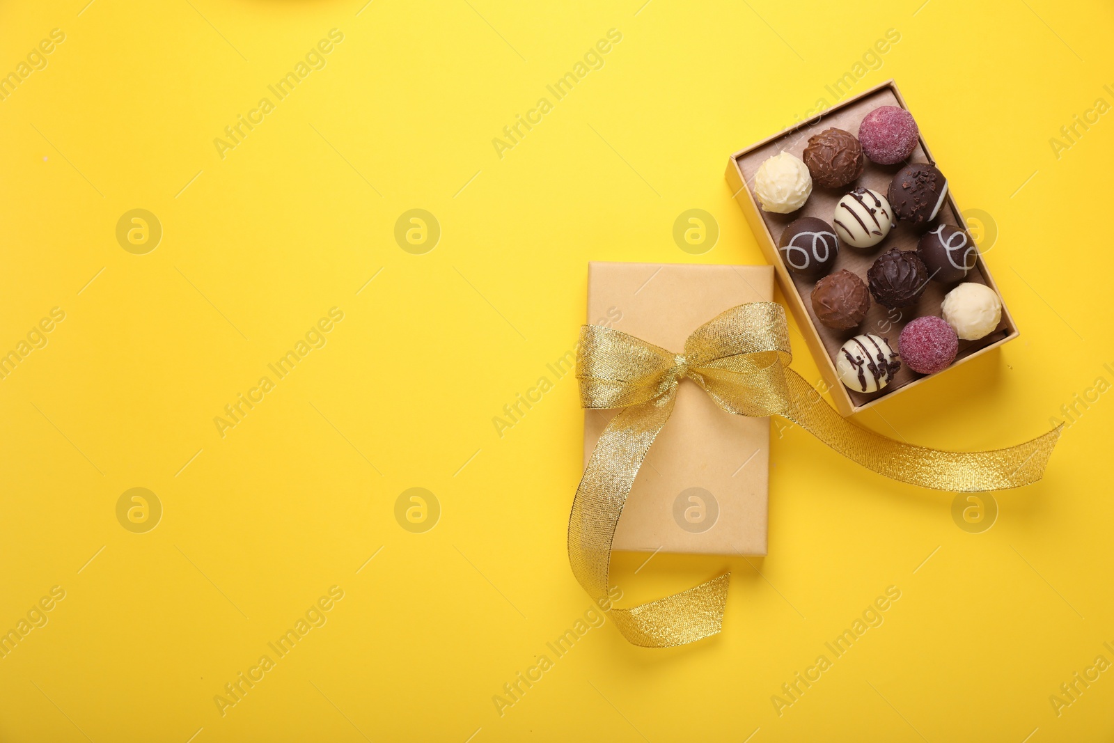 Open box with delicious chocolate candies on yellow background, top view. Space for text Photo of Open box with delicious chocolate candies on yellow background, top view. Space for text
