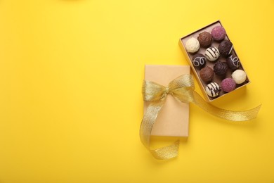 Photo of Open box with delicious chocolate candies on yellow background, top view. Space for text