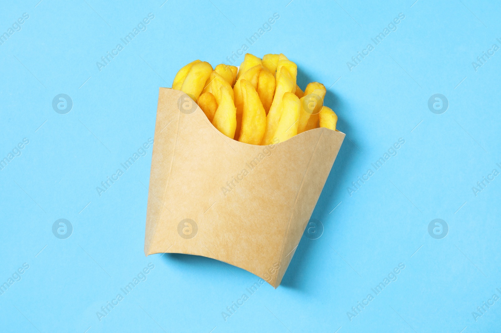 Photo of Paper cup with French fries on light blue table, top view