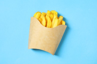 Paper cup with French fries on light blue table, top view