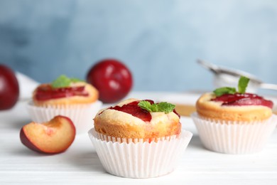 Photo of Delicious cupcakes with plums on white wooden table, closeup