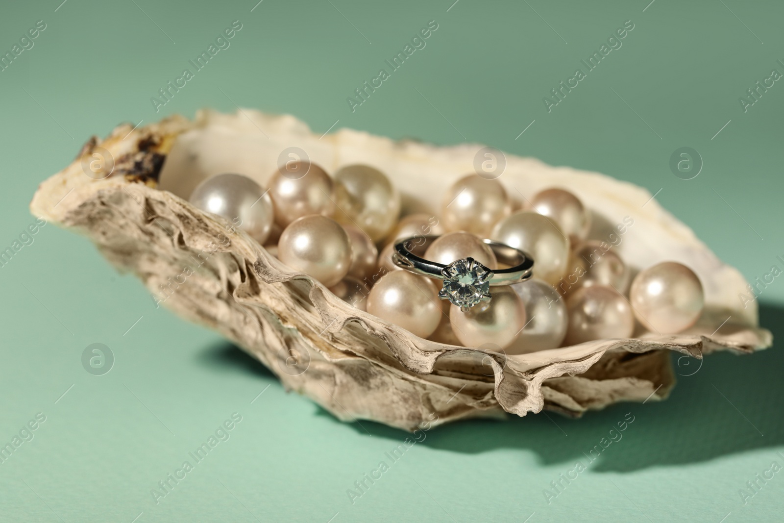 Photo of Beautiful engagement ring with gemstone and pearls in shell on mint background