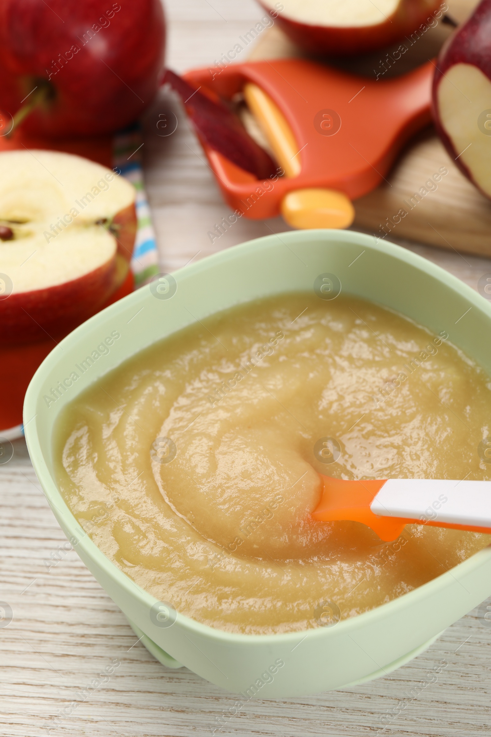 Photo of Healthy baby food. Bowl with delicious apple puree and fresh fruits on white wooden table