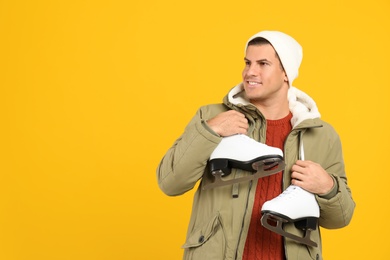 Photo of Happy man with ice skates on yellow background. Space for text