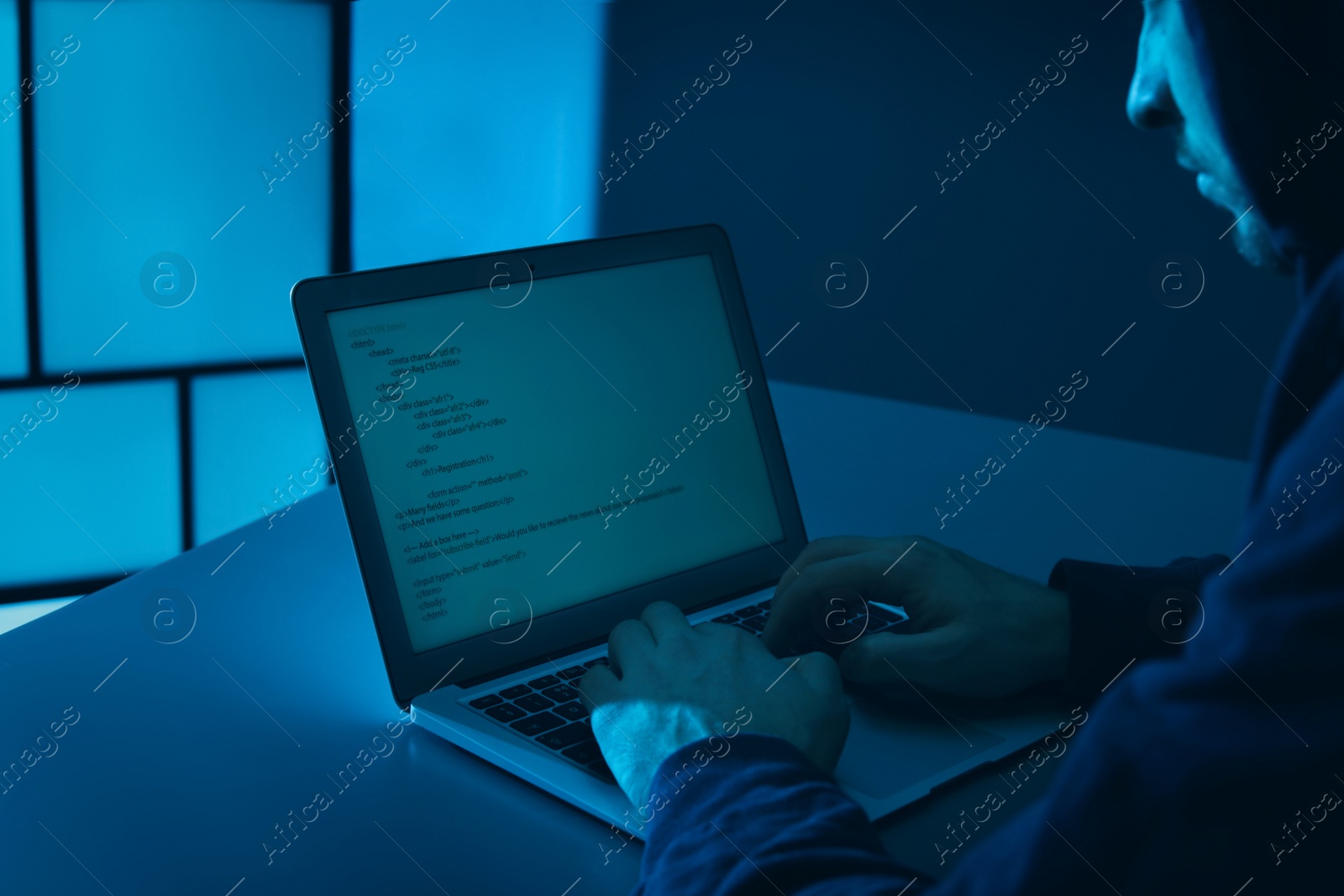 Photo of Man using laptop at table in dark room, closeup. Criminal offence