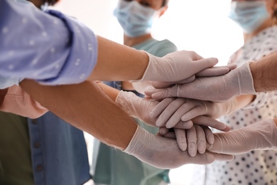 Photo of People in white medical gloves stacking hands on light background, closeup