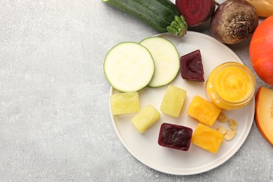 Photo of Frozen beet, pumpkin and zucchini puree cubes with ingredients on light grey table, flat lay. Space for text