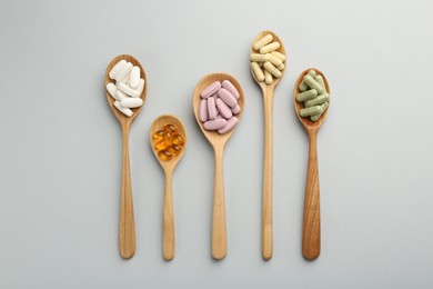 Photo of Different vitamin pills in spoons on light grey background, flat lay. Health supplement