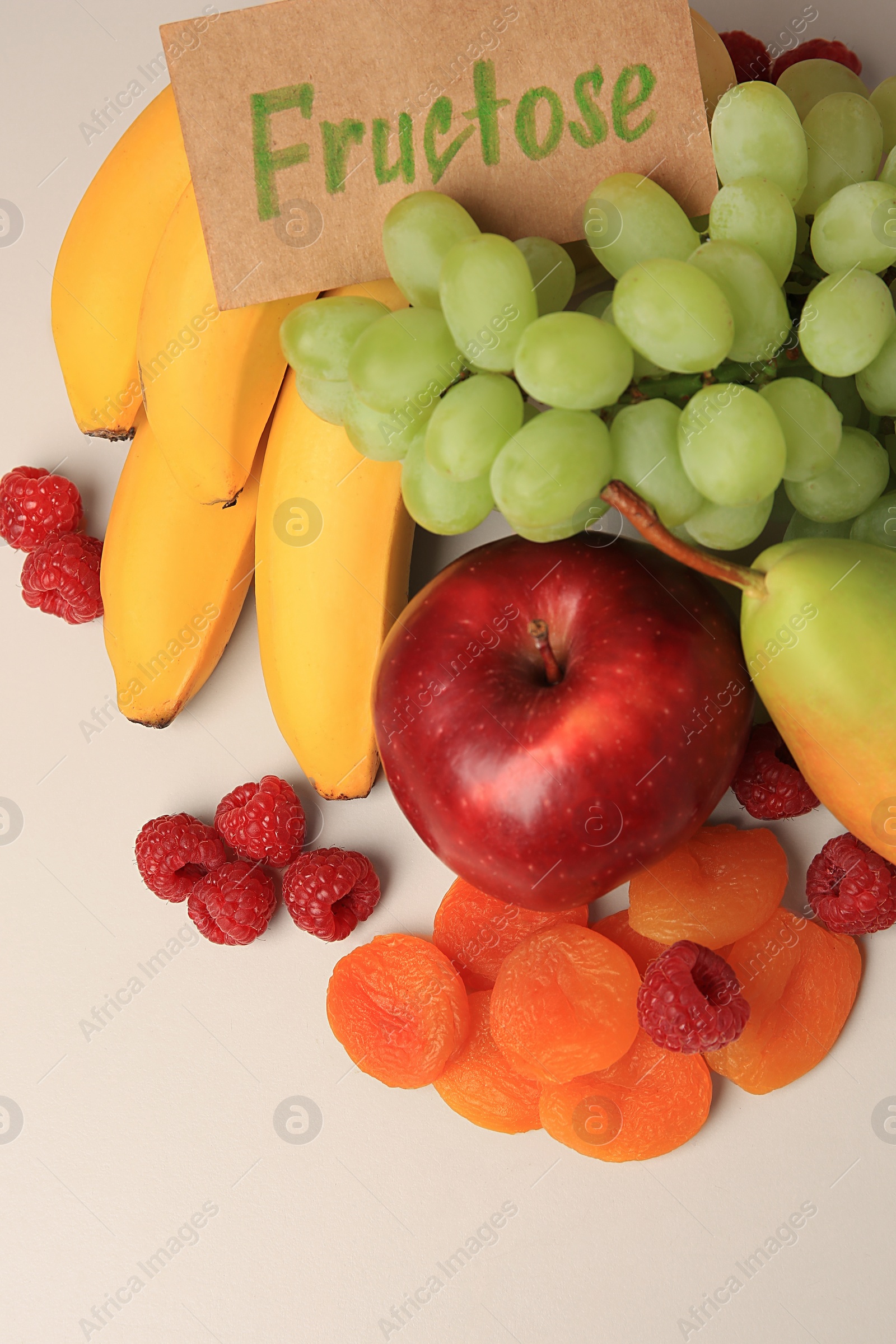 Photo of Card with word Fructose, delicious ripe fruits, raspberries and dried apricots on beige table, above view