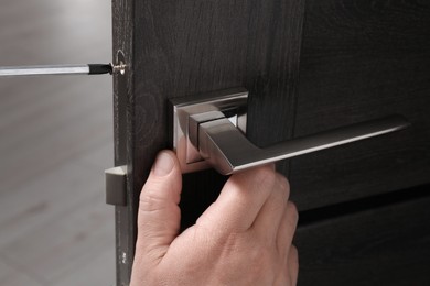 Photo of Handyman with screwdriver repairing door handle indoors, closeup